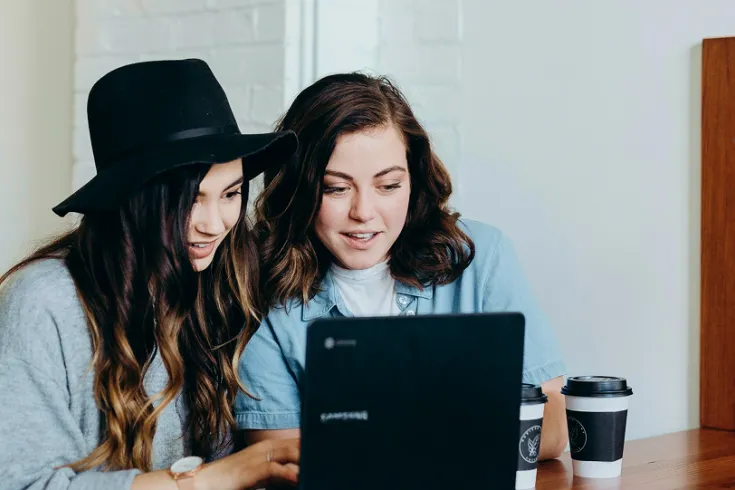 Two students sat at a table looking at a laptop