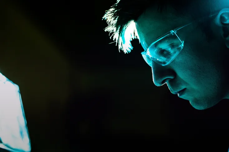 Photo of a man wearing protective glasses, looking at a screen with a futurist green glow