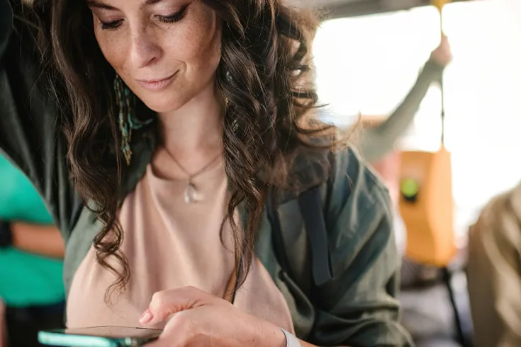 Woman standing while travelling on a bus looking at a phone in her hand.