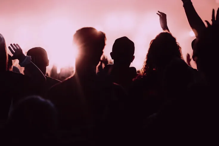 A view from behind of fans watching a stage under a pink glow