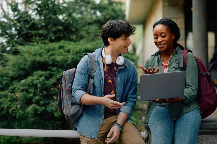 Two students sat on a wall looking at a laptop