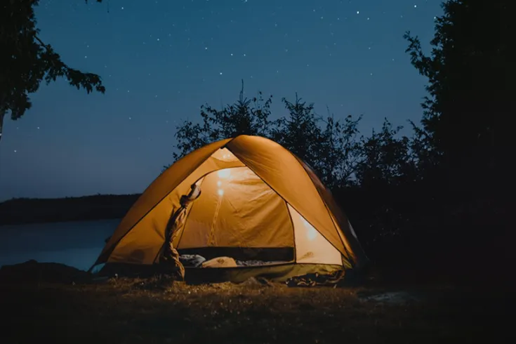 A cosy tent lit from inside in a forest landscape at nighttime.