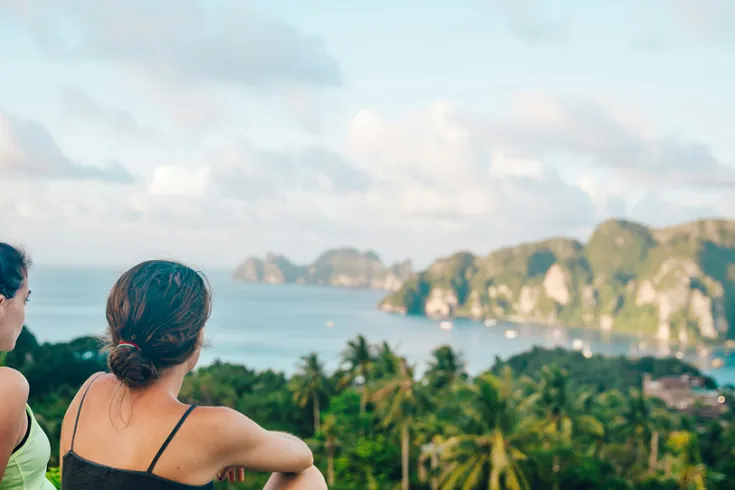 Two women sat on a hill looking out over a tropical bay