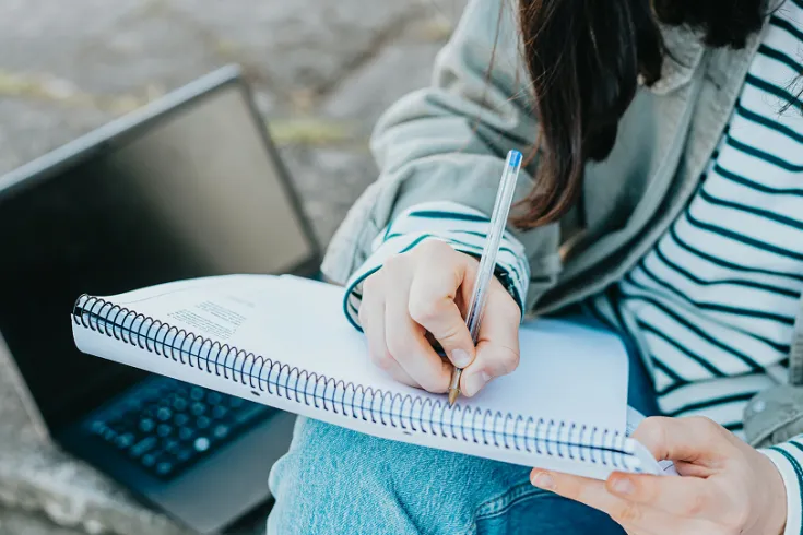 Close up of a students hands writing in a notebook