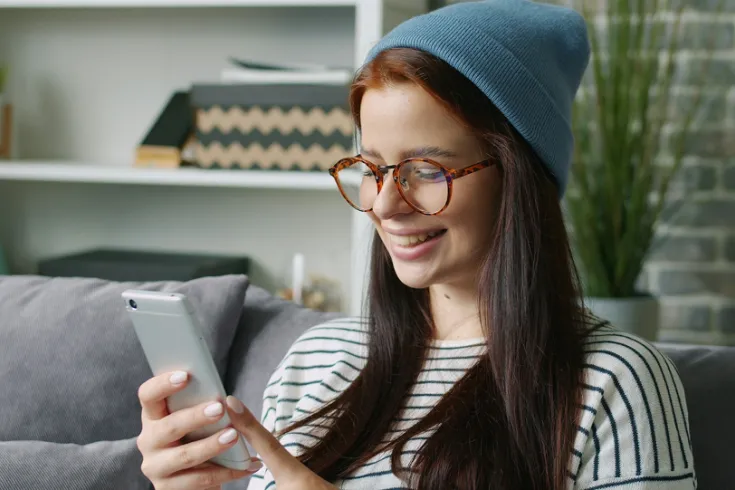 A student sitting on a sofa smiling and looking at a phone.