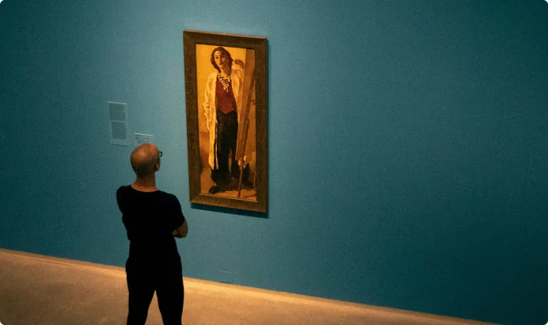 A man looking at a piece of art in a gallery, the view is of his back looking forwards the art.