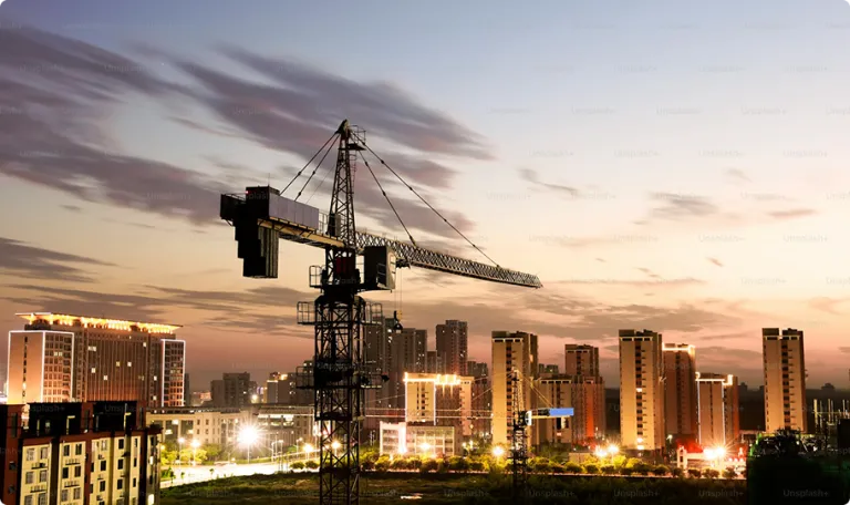 A crane over a skyline of lit-up buildings at sunset