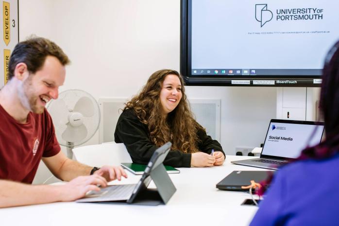 University students laughing, Portsmouth logo in the background