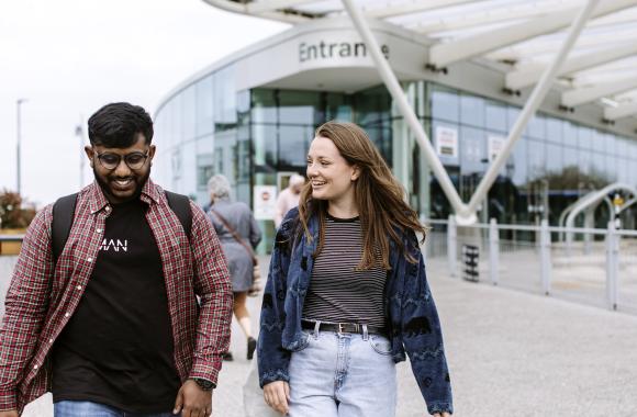 Two students walking with the campus in the background