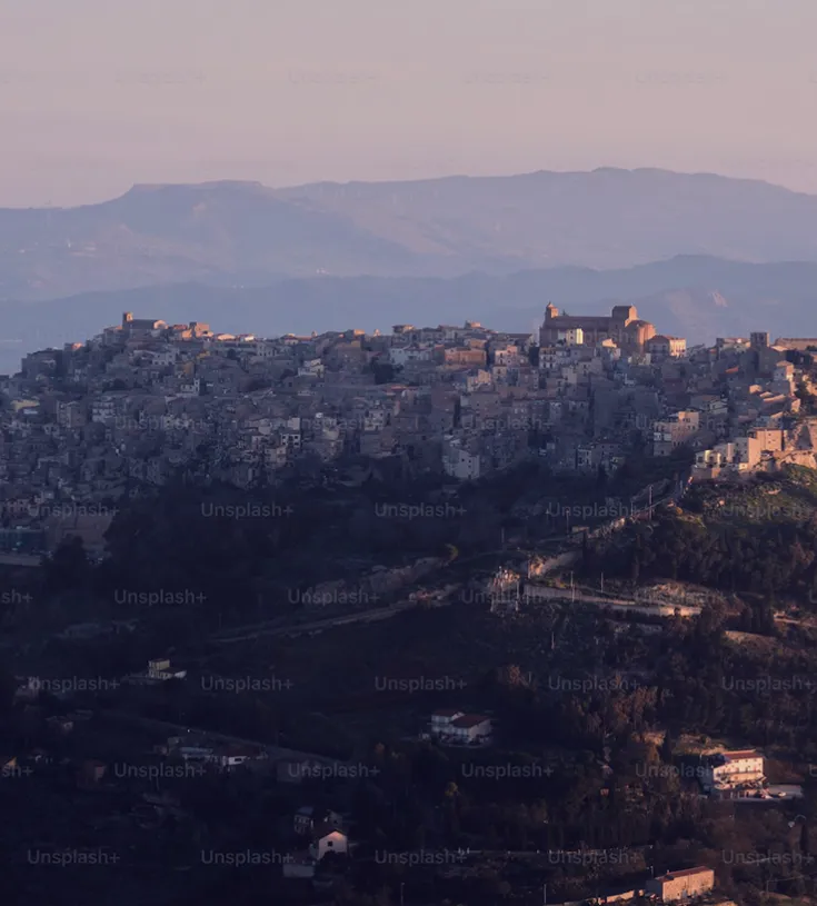 A village on top of a hill with mountains in the background.