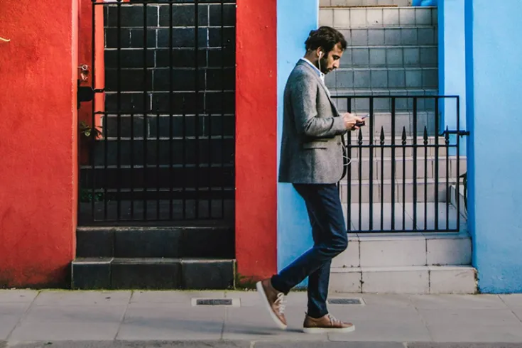 Man walking along a street of bright coloured building with earphones in